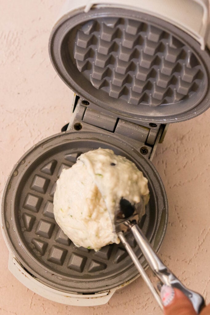 Waffle batter being spooned onto a hot waffle maker