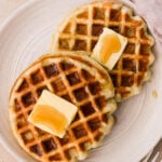 Fluffy ricotta waffles stacked on a plate with syrup drizzle and butter