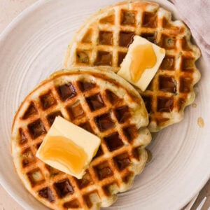 Fluffy ricotta waffles stacked on a plate with syrup drizzle and butter