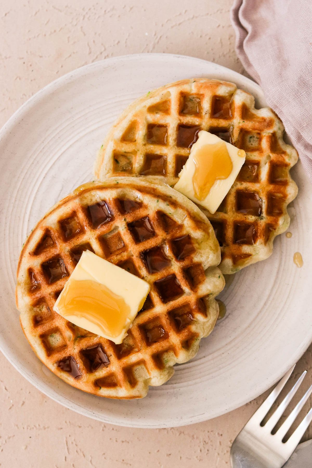 Fluffy ricotta waffles stacked on a plate with syrup drizzle and butter