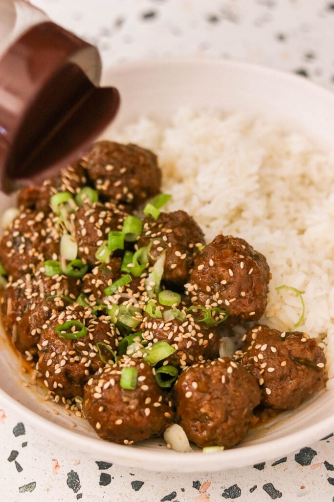 korean bbq meatballs garnished with green onions and sesame seeds on a plate with white rice