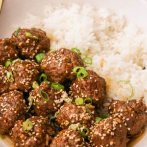 korean bbq meatballs garnished with green onions and sesame seeds on a plate with white rice