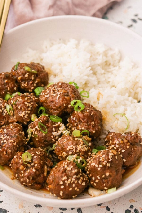 korean bbq meatballs garnished with green onions and sesame seeds on a plate with white rice