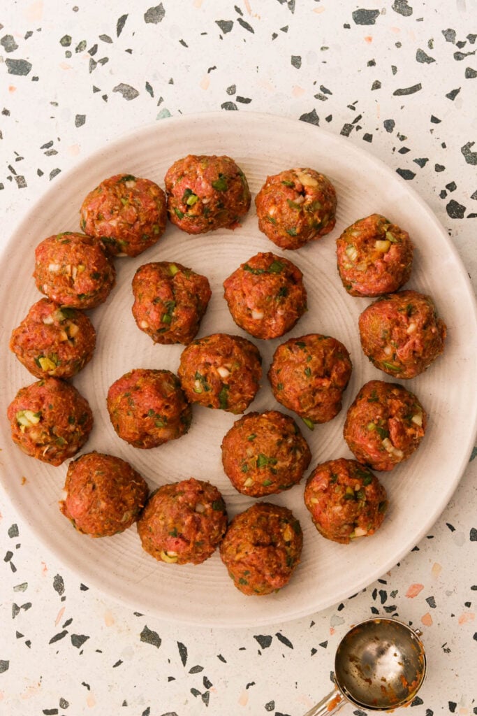 golfball shaped meatballs raw on a white plate ready to chill