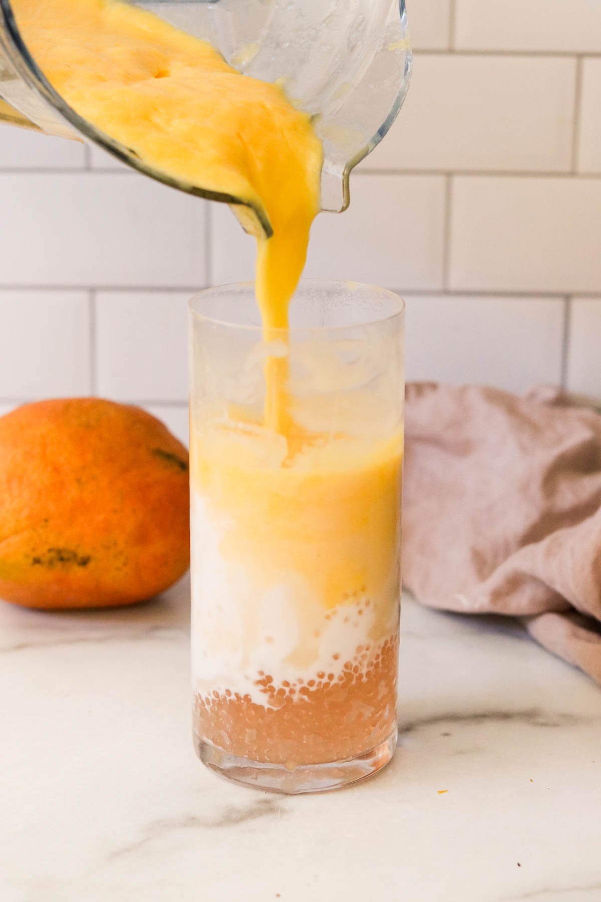 Pouring mango smoothie mixture into prepared glass with pearls and coconut milk.
