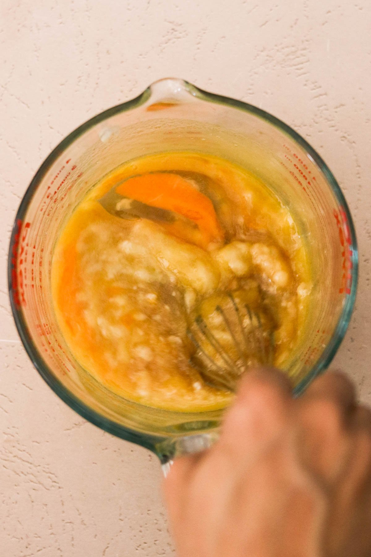 Wet ingredients—mashed banana, maple syrup, melted butter, egg, and vanilla—being whisked in a glass measuring cup.