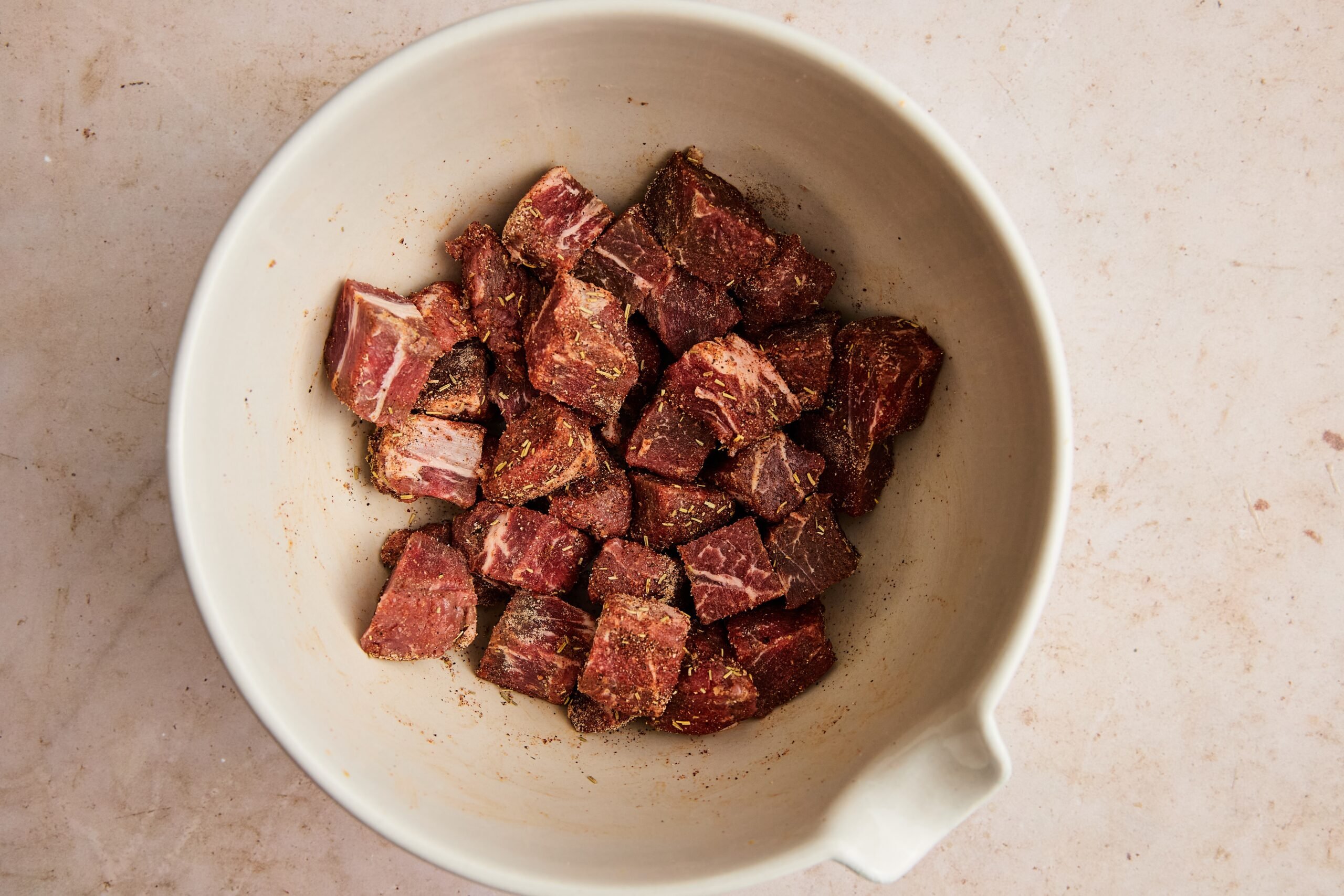 Cubed beef in a bowl tossed with salt, onion powder, garlic powder, thyme, paprika, and pepper.