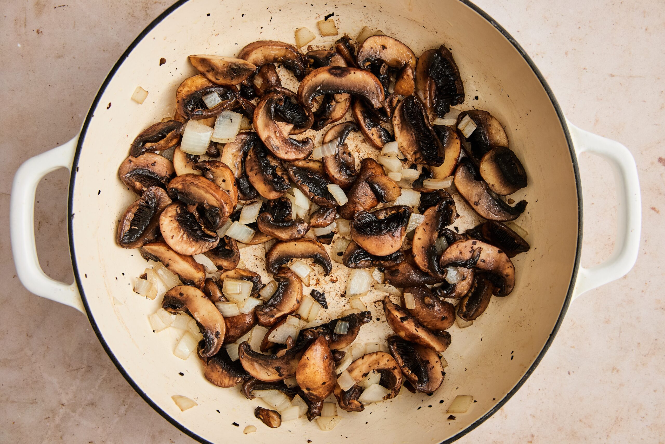 Sliced onions and mushrooms sautéing in ghee in a Dutch oven.