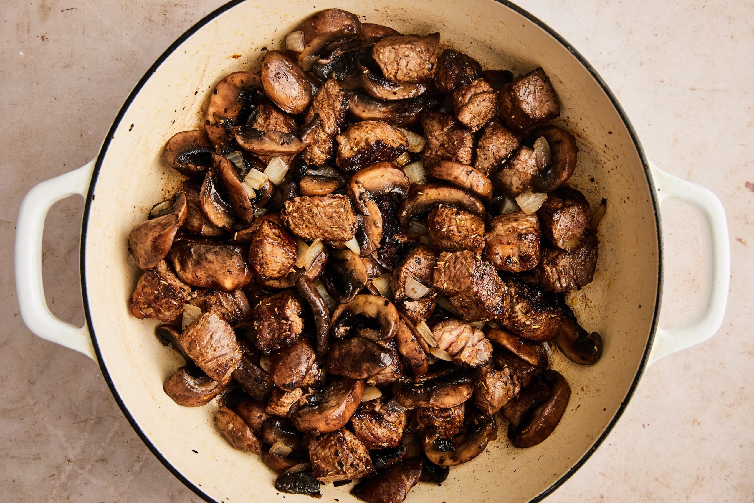 Seasoned beef searing in a hot skillet, with mushrooms, onion, and ghee, browning on all sides.