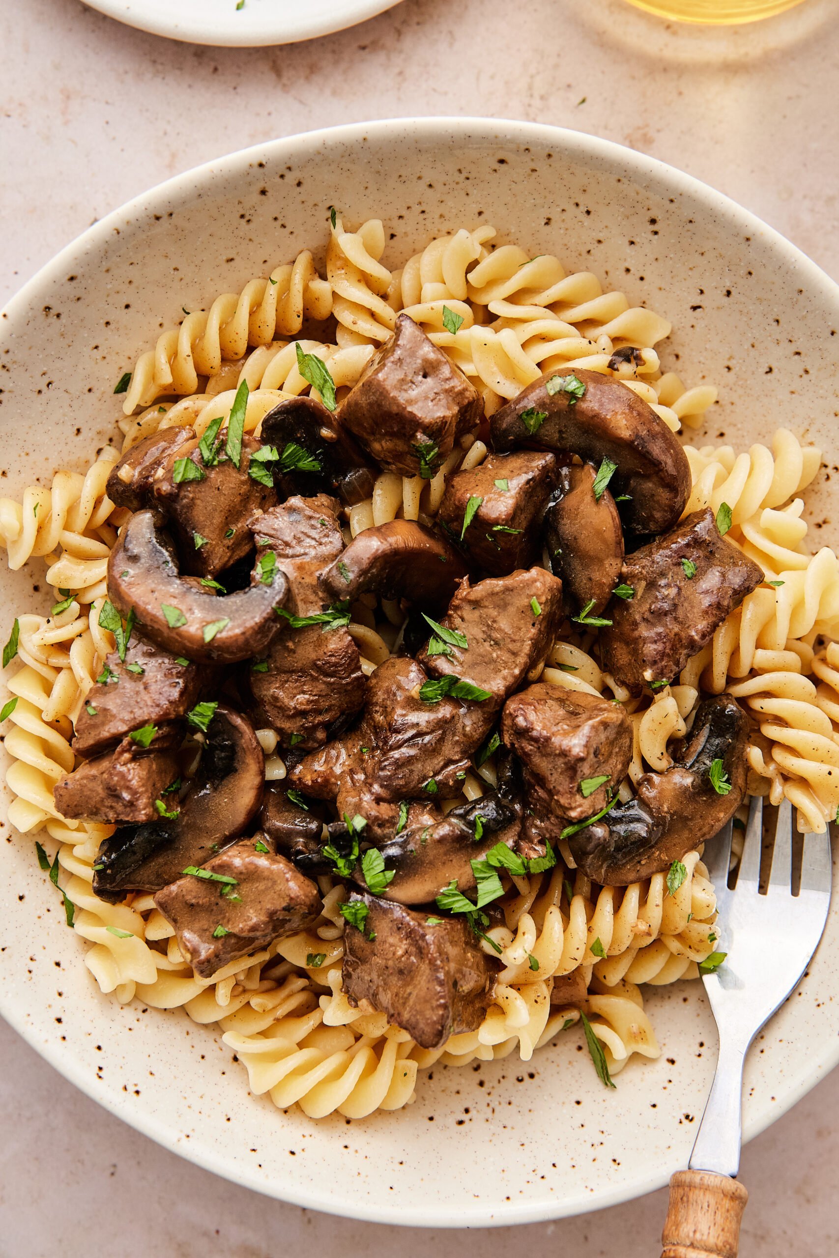 Bowl of dairy-free beef stroganoff with tender beef, mushrooms, and creamy sauce over pasta, sprinkled with parsley.
