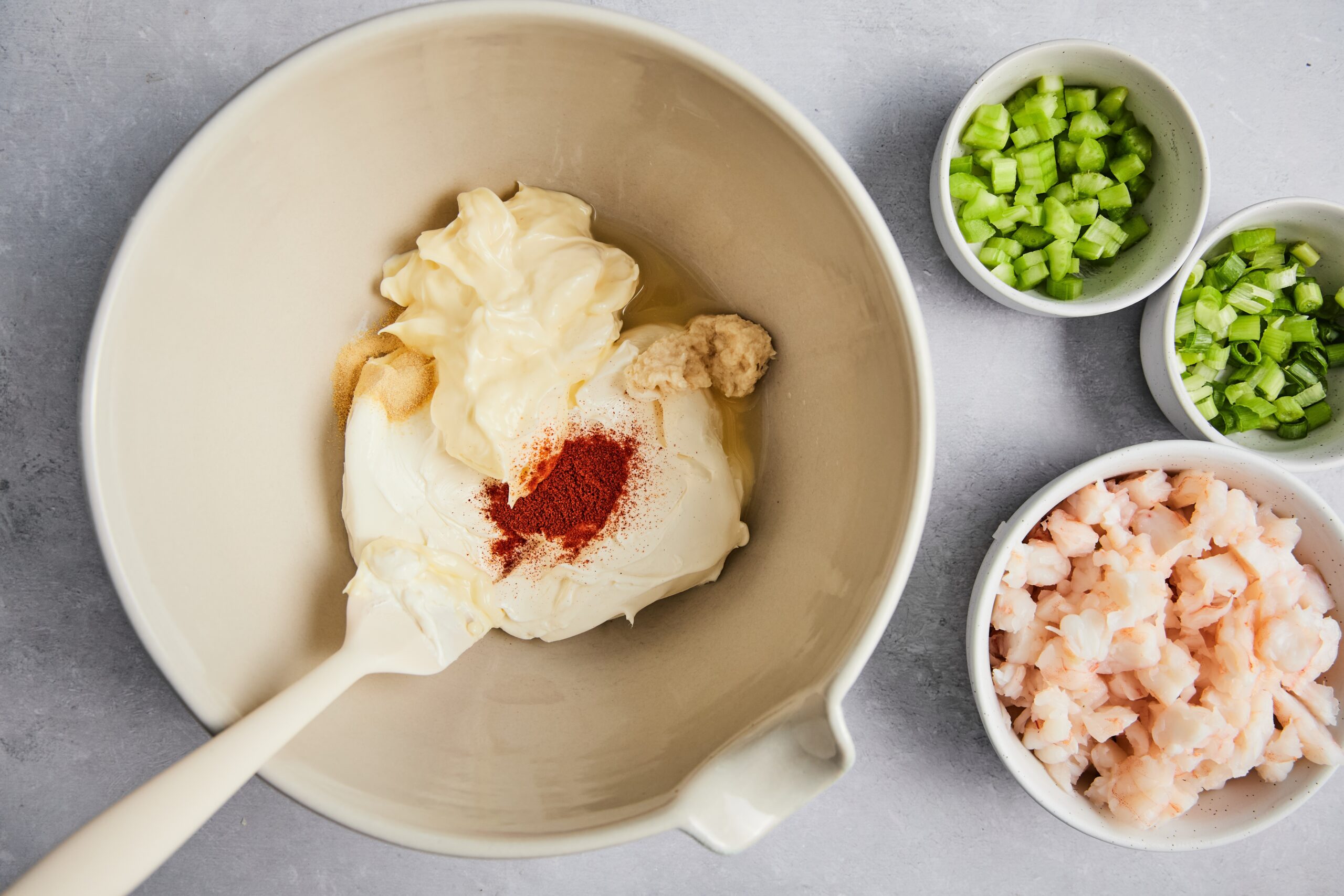 Cream cheese, mayo, lemon juice, horseradish, paprika, and garlic powder being mixed in a white bowl.