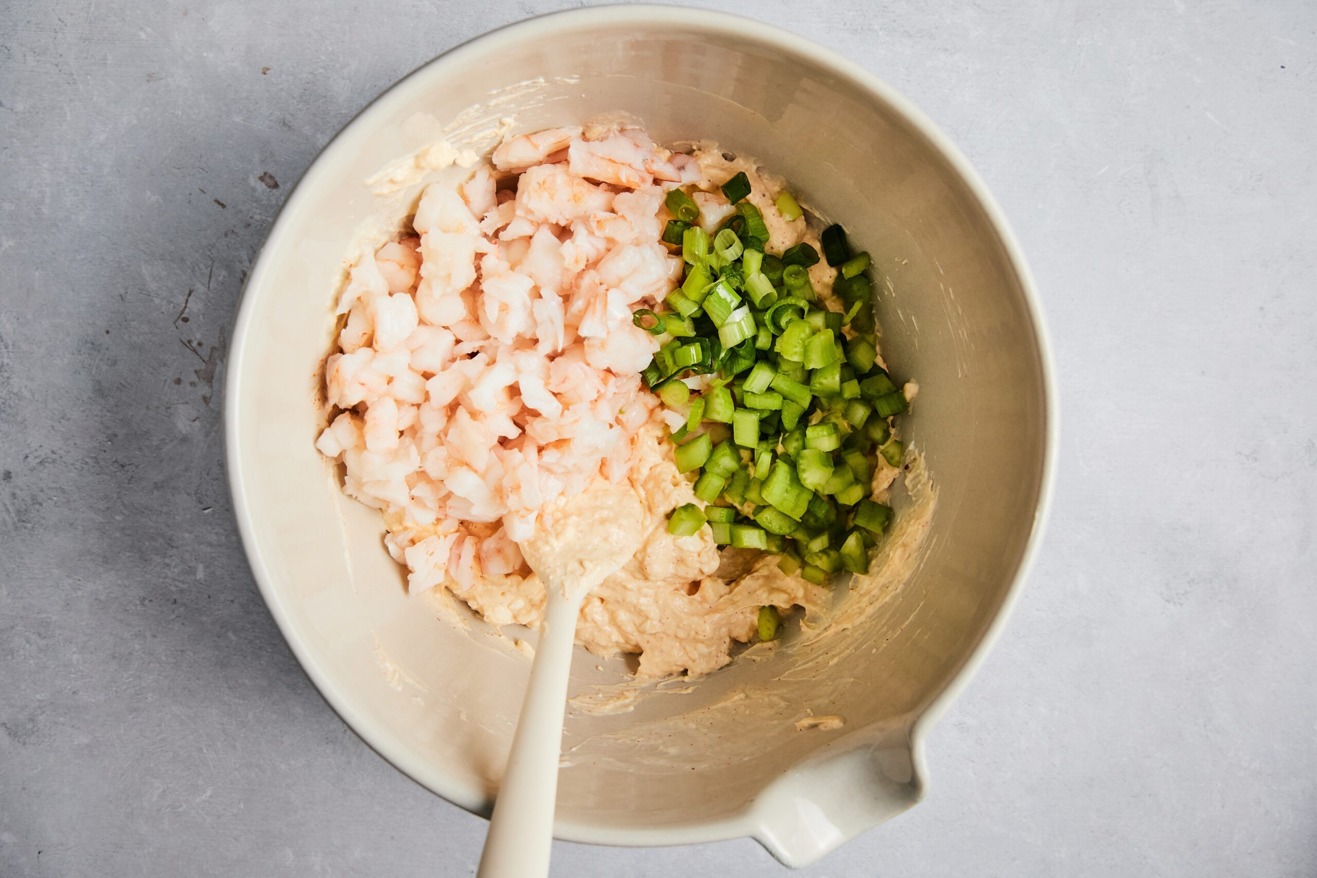 Chopped shrimp, celery, and green onions being folded into the creamy base.