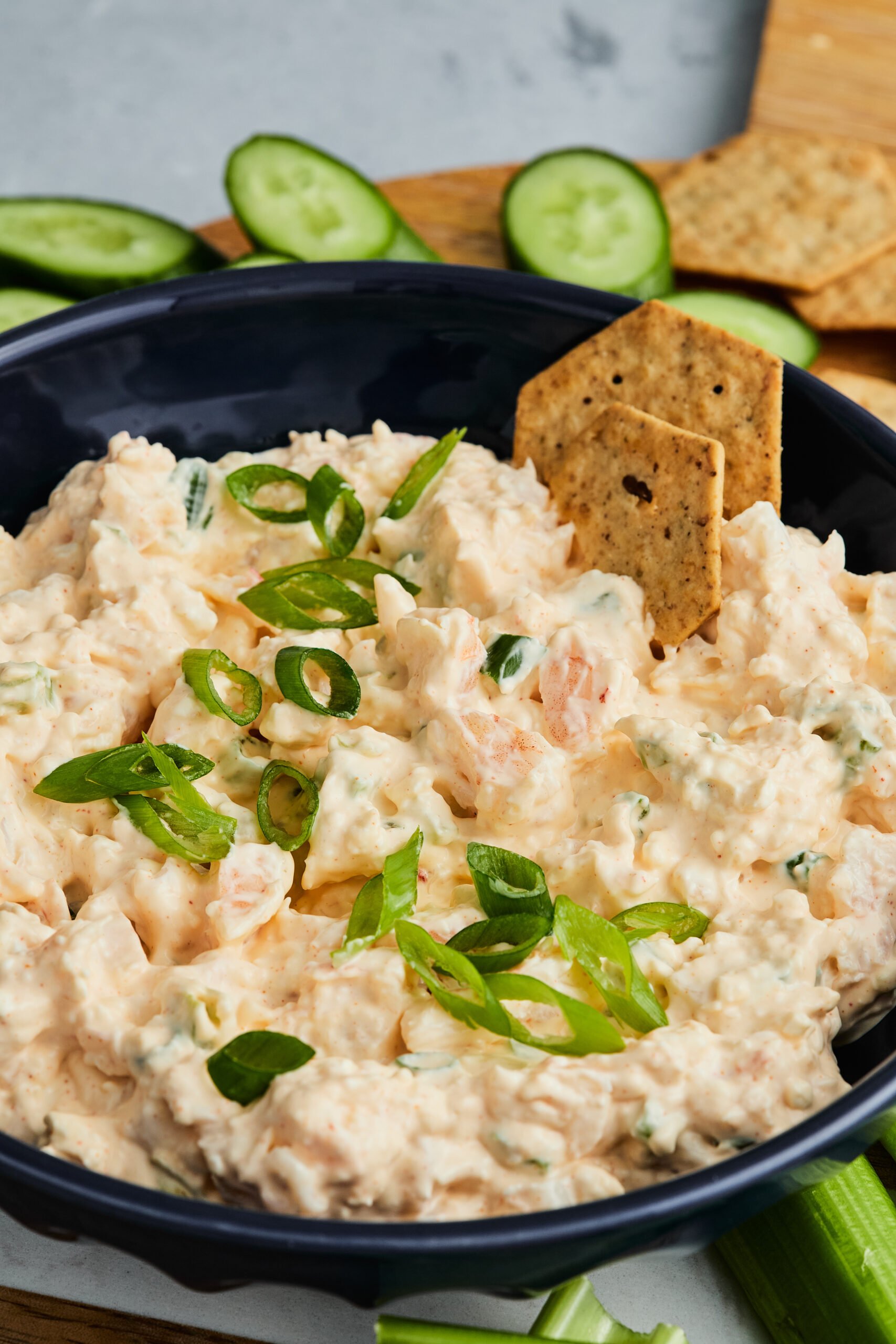 Bowl of creamy shrimp dip topped with green onions, served with crackers and veggie dippers.
