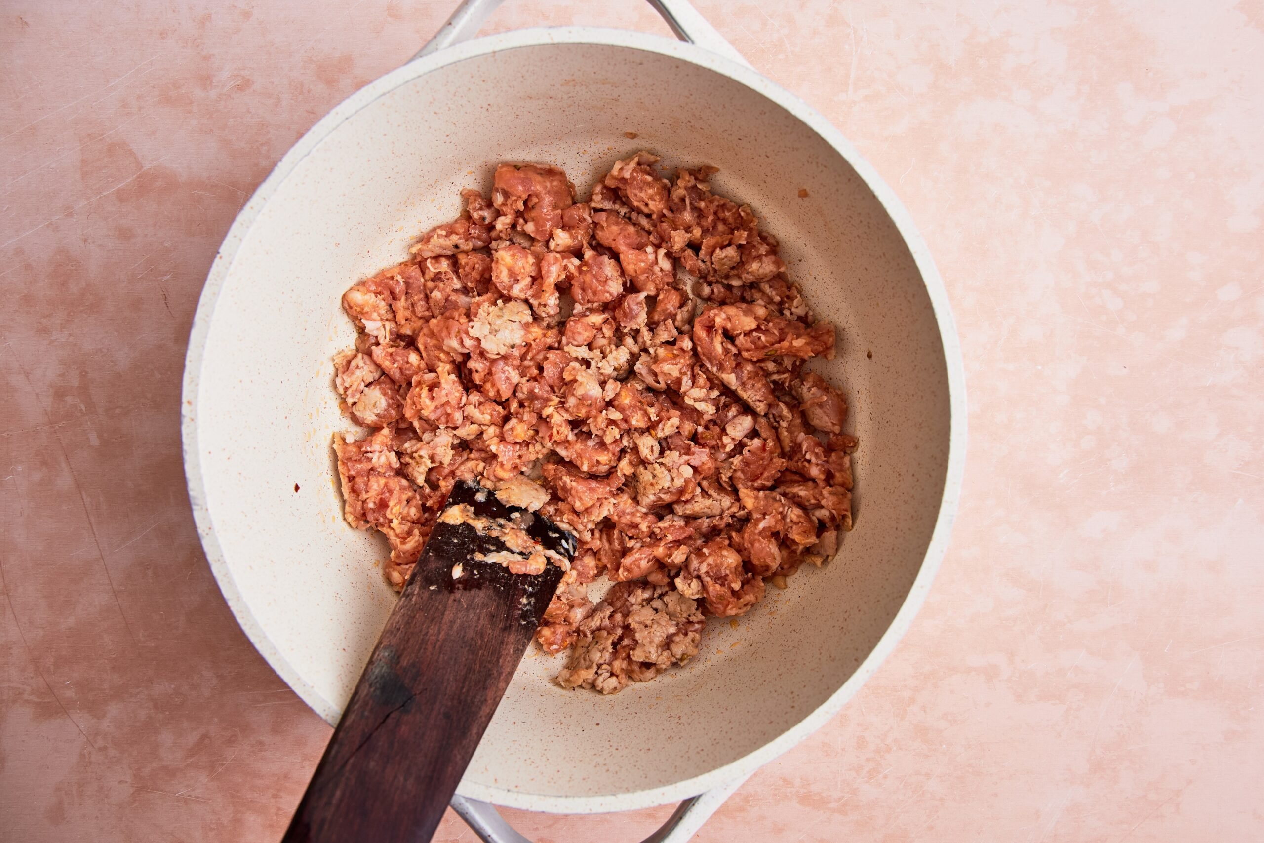 Italian sausage being browned in a large white soup pot.