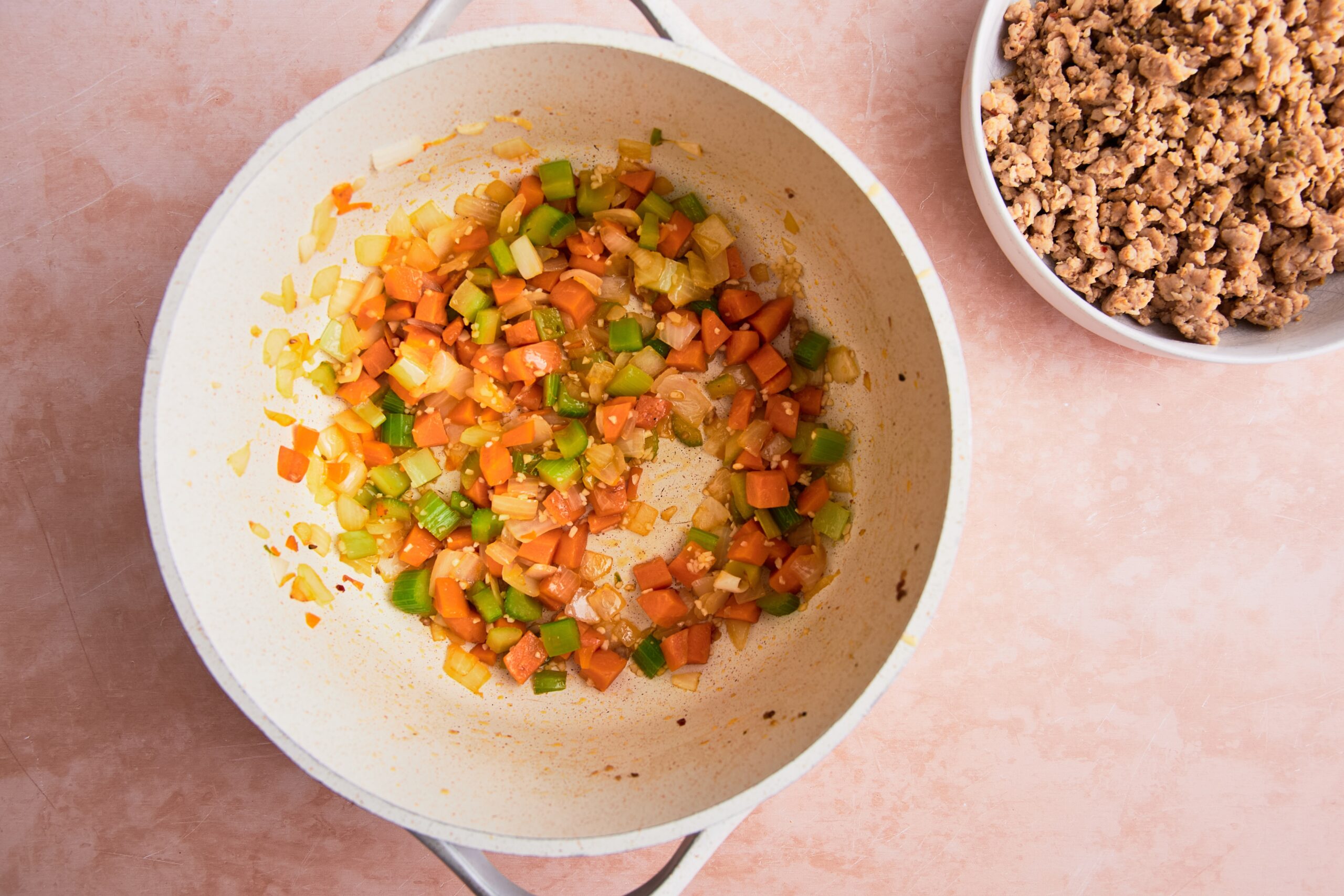 Chopped onions, carrots, and celery sautéing in a pot with garlic; the browned meat sitting in a small bowl beside it.