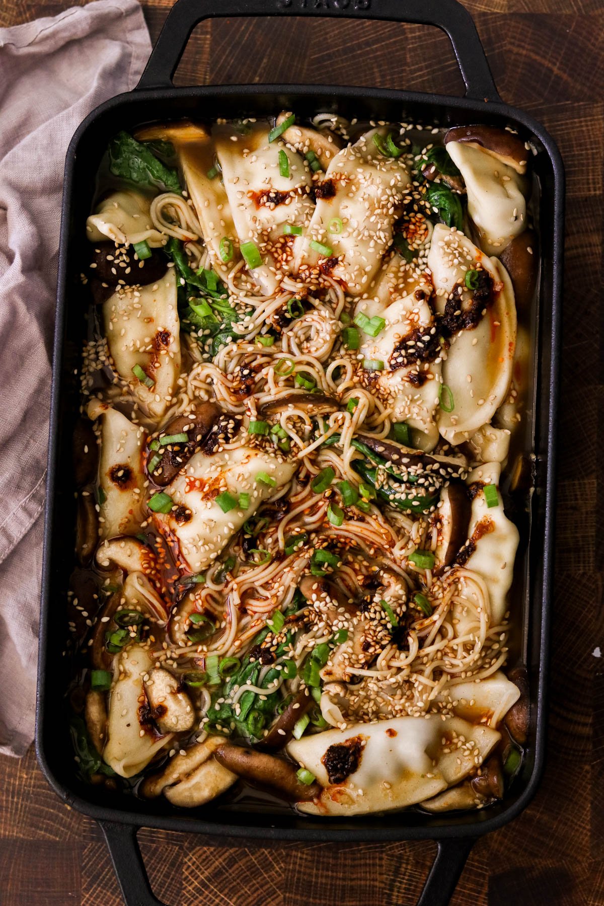Overhead view of baked dumplings with ramen in a gochujang broth, garnished with green onions and sesame seeds in a baking dish.