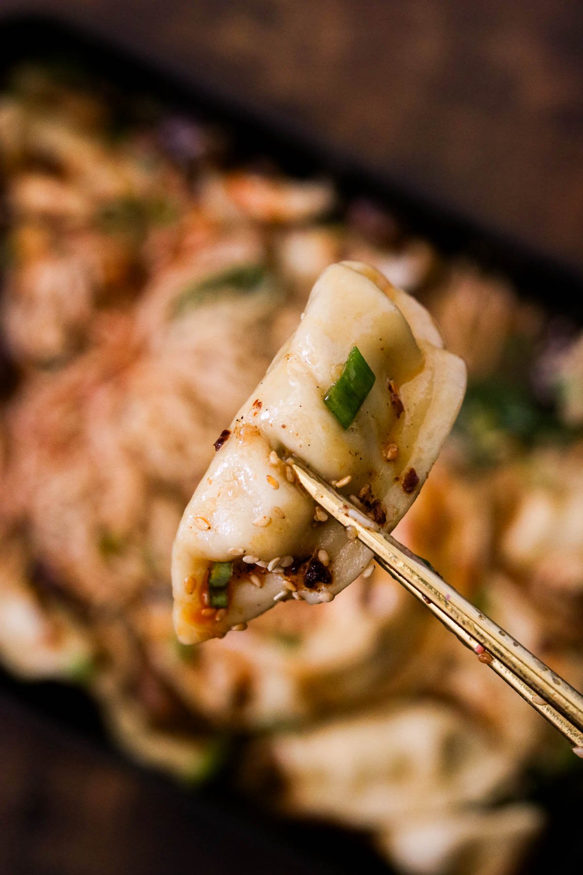 Close-up of a baked dumpling being help between two chopsticks.