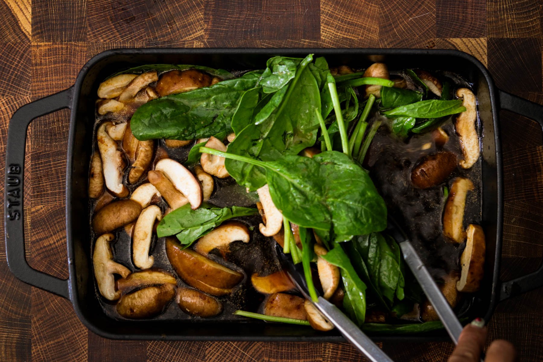 Fresh mushrooms and spinach added to the gochujang broth in a baking dish.