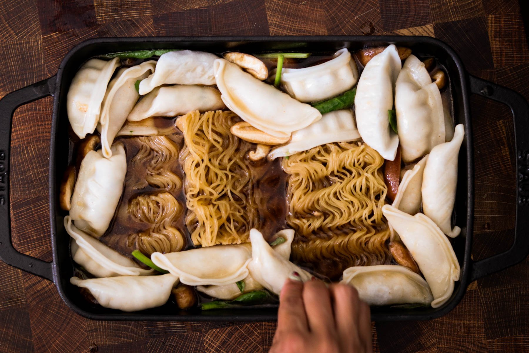 Ramen cakes and frozen dumplings arranged in a baking dish with broth.