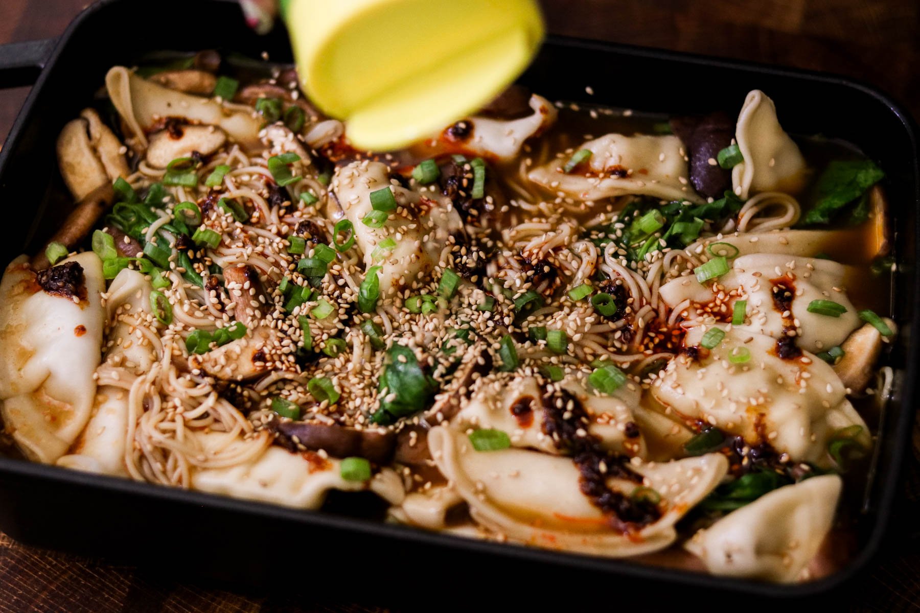 Finished baked dumplings and ramen garnished with green onions, sesame seeds, and chili oil in a baking dish.
