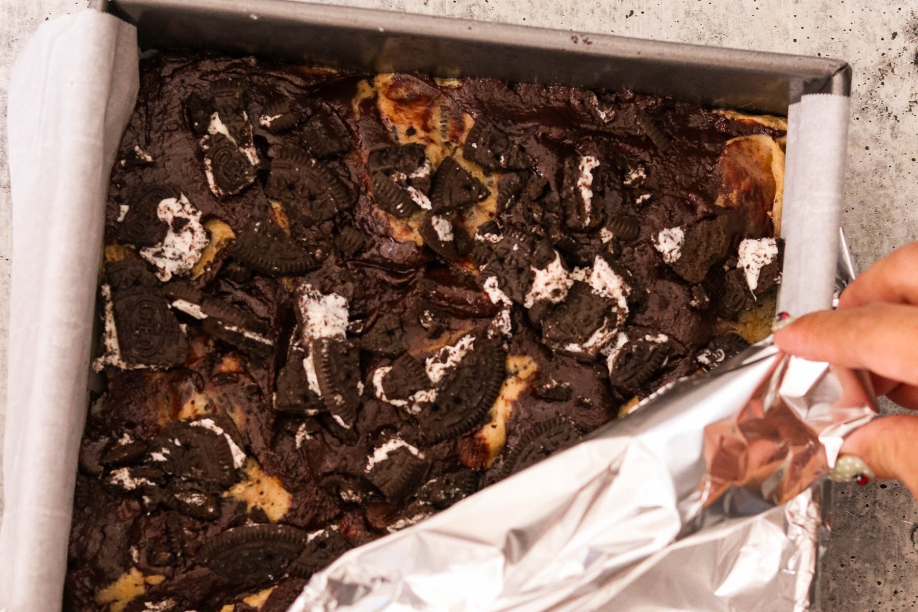 Baked Oreo brookies topped with chopped Oreos in a parchment-lined pan.
