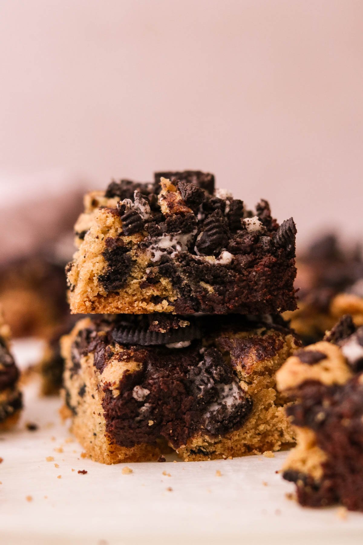 Close-up of two stacked Oreo brookies against a light pink backdrop, showing fudgy brownie, chewy cookie layers, and Oreo pieces.