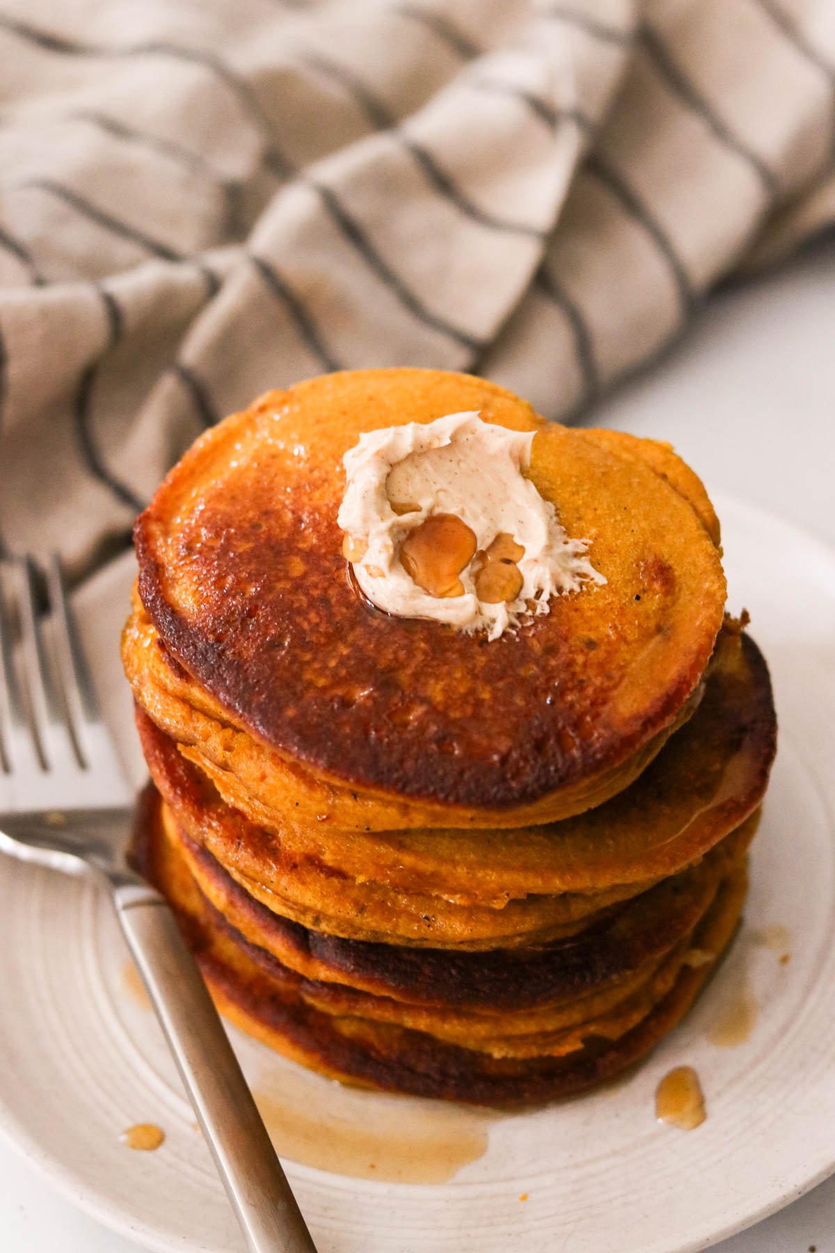 Close-up of fluffy pumpkin protein pancakes topped with cinnamon maple butter and syrup.