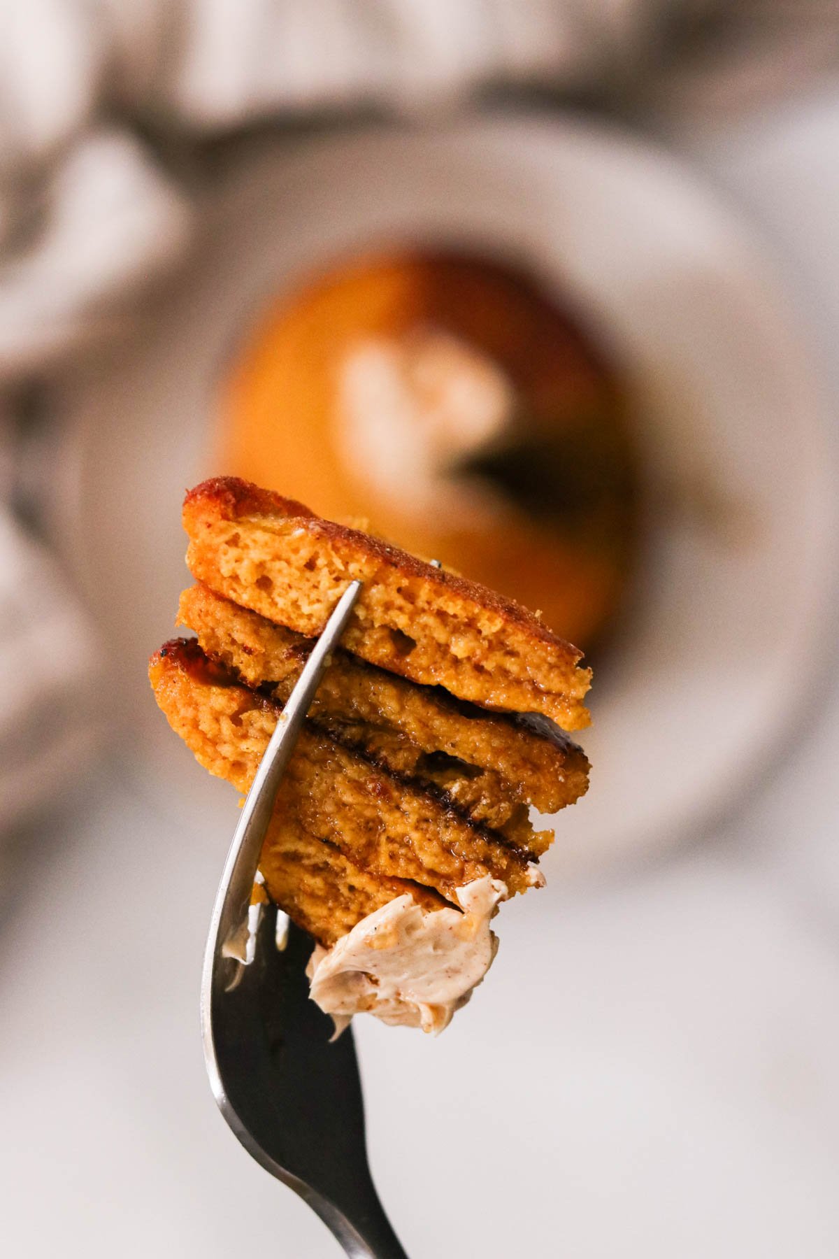 Close-up of pumpkin protein pancakes cut into pieces on a fork with cinnamon maple butter spread on the side.