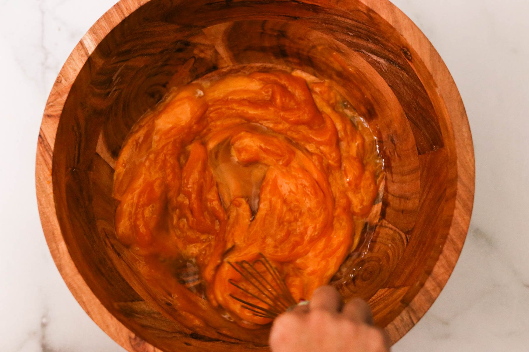 Eggs and pumpkin puree being whisked in a large wooden mixing bowl.