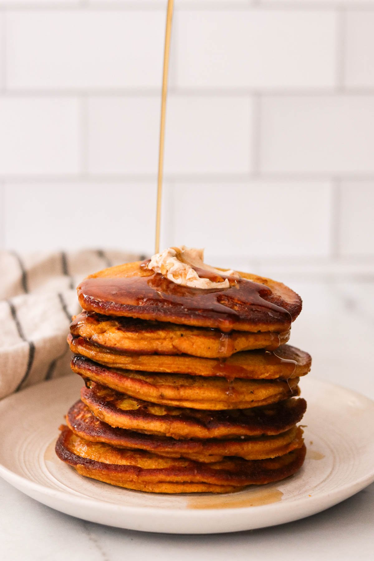 Stack of fluffy pumpkin protein pancakes topped with cinnamon maple butter and maple syrup.
