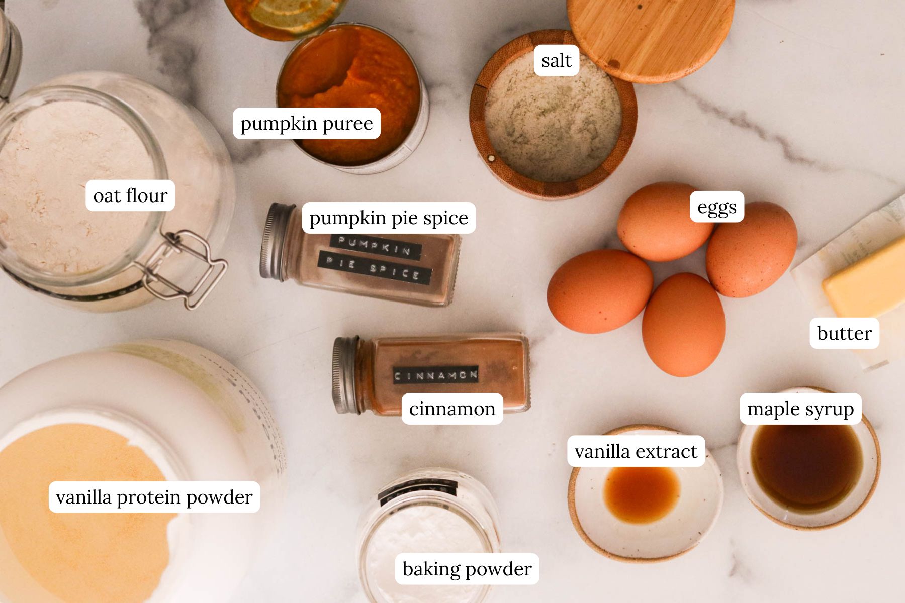 Pumpkin protein pancake ingredients laid out on a table, including pumpkin puree, oat flour, protein powder, eggs, and spices.