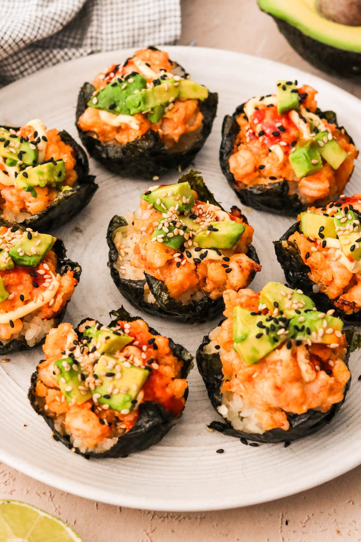 Close-up of plated shrimp sushi cups topped with avocado and sesame seeds served on a white dish.