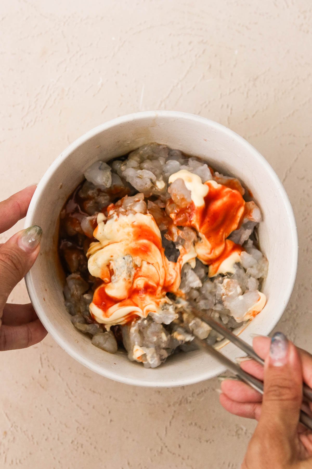 Hands mixing chopped shrimp with Kewpie mayo, sriracha, tamari, and lime juice in a small white bowl for sushi cup filling.