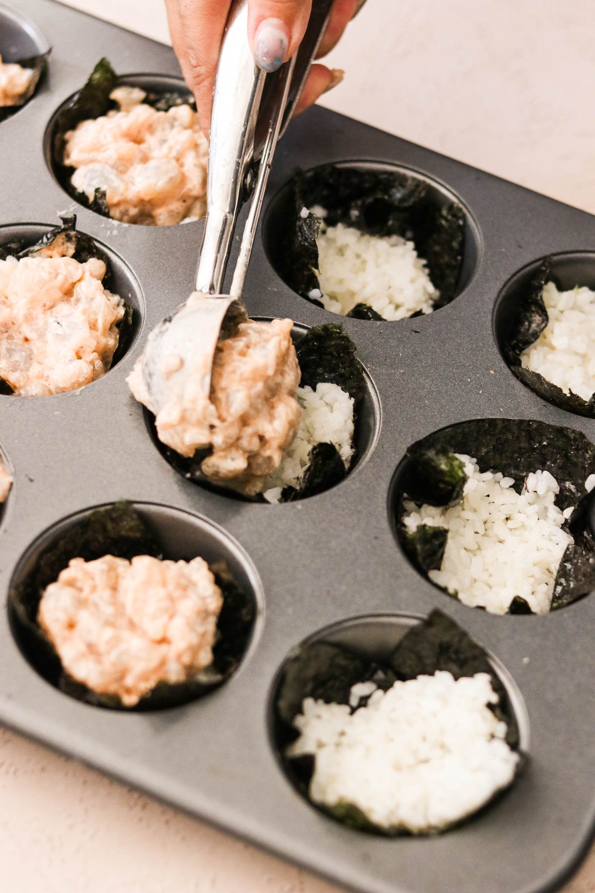 Shrimp mixture spooned on top of rice in nori-lined muffin tin cups before baking.