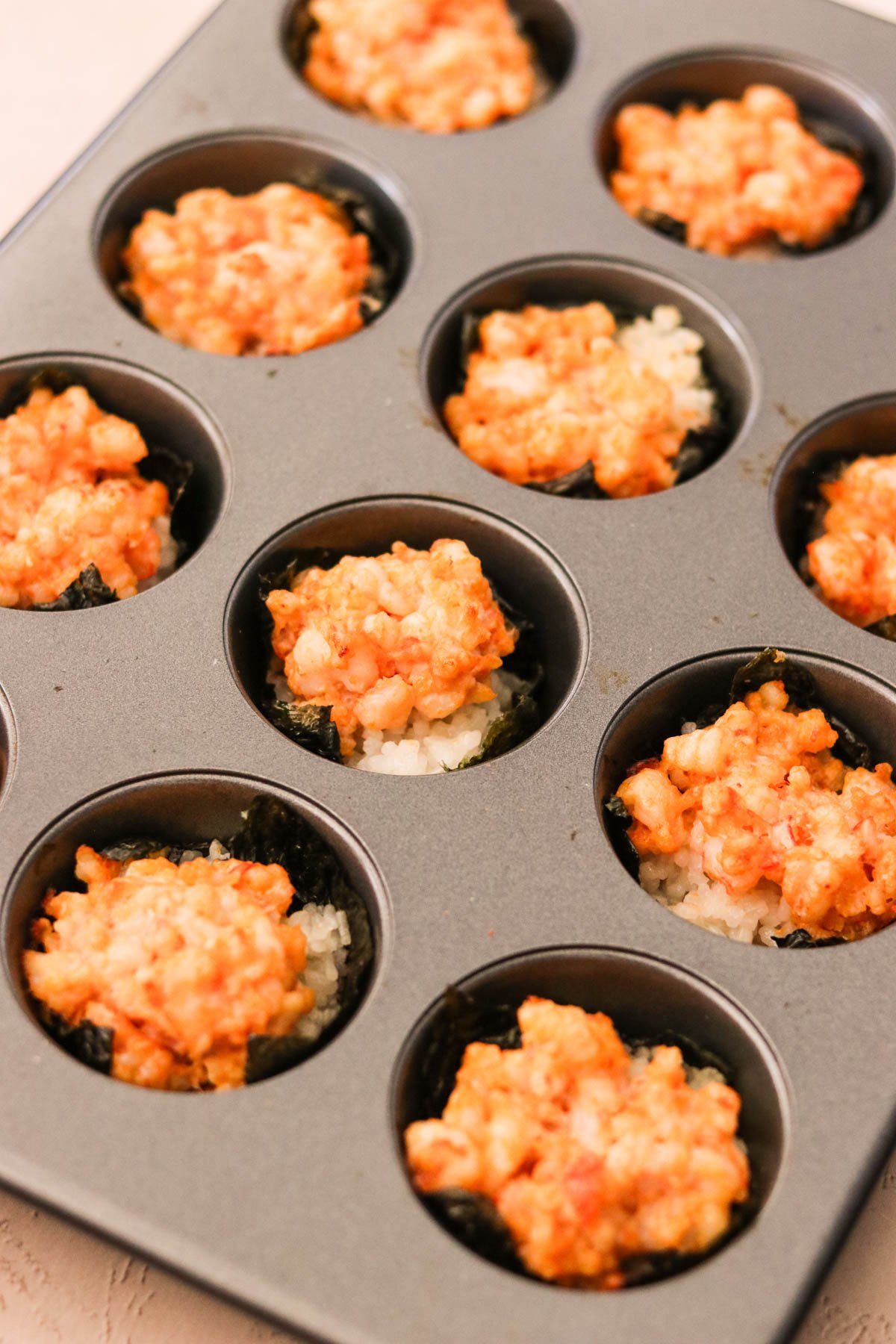 Sushi cups ready to bake in the oven with shrimp filling on top of the rice.