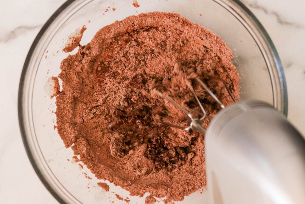 Using a hand mixer to whisk in wet ingredients to dry ingredients for chocolate cake
