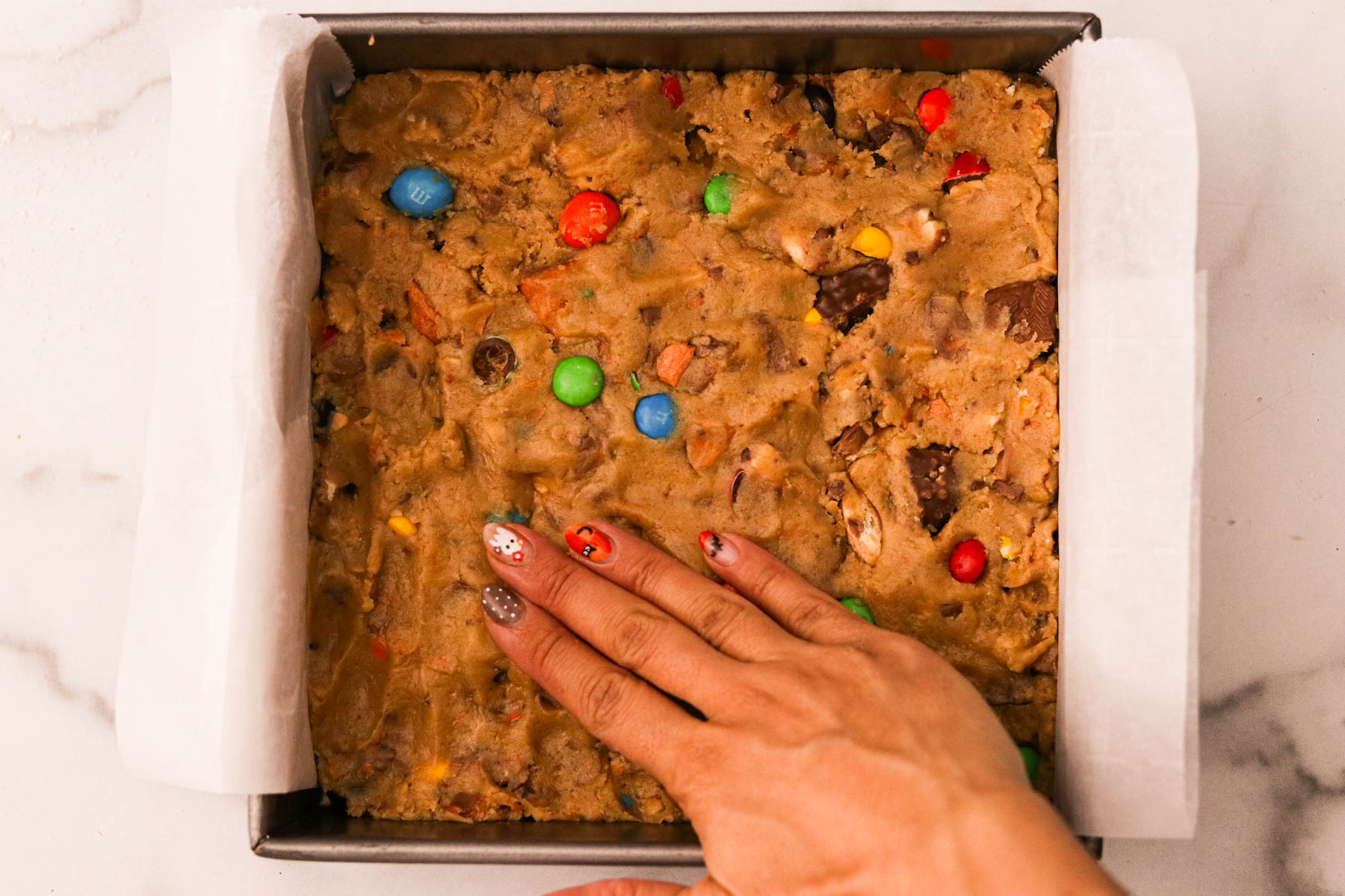 A hand pressing dough mixture evenly into a parchment lined pan.