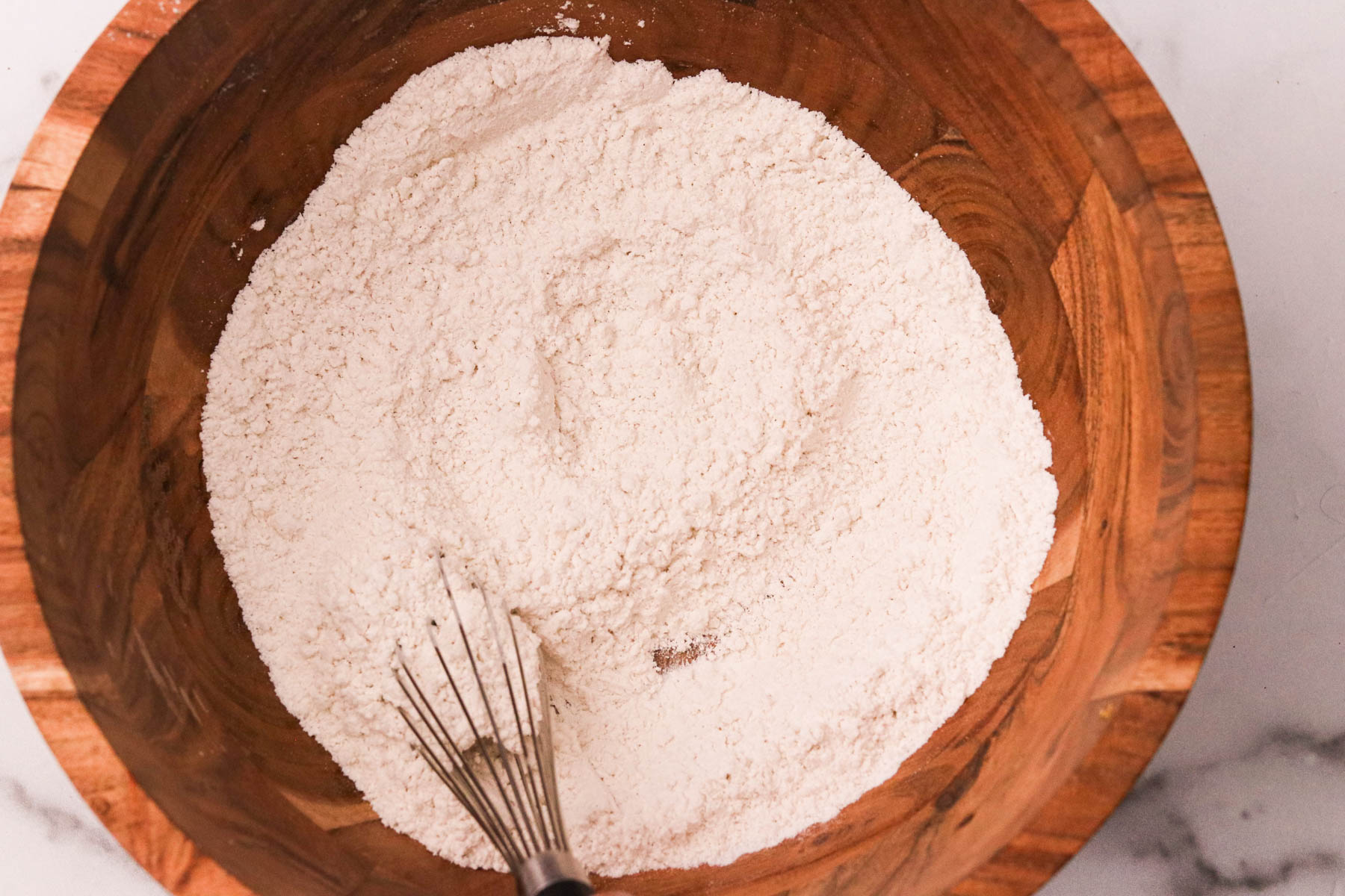 Flour, baking powder, and sea salt being whisked together in a large mixing bowl.