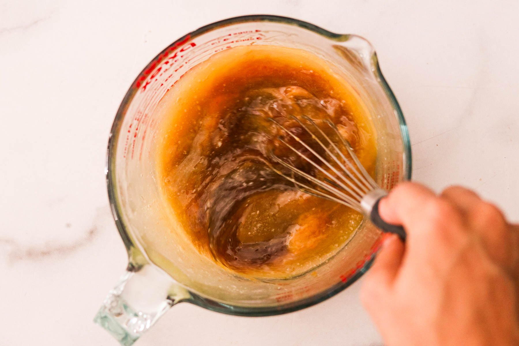 Butter, brown sugar, egg, egg yolk, and vanilla extract in a glass measuring cup being whisked together.