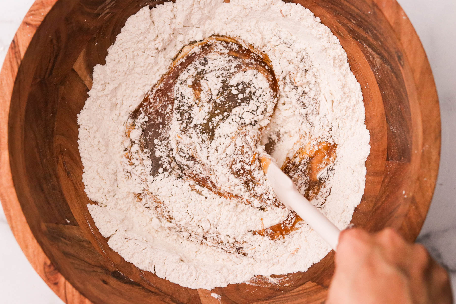 Wet ingredients being stirred into the dry mixture in a large wooden  bowl.
