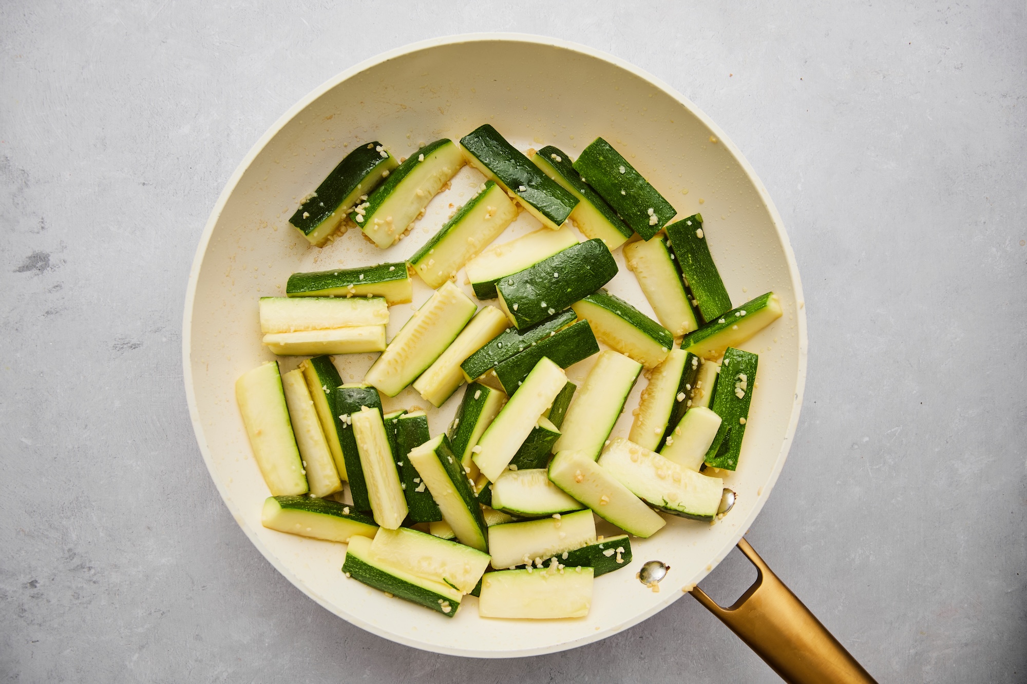 Zucchini sticks added to the large white skillet with avocado oil and garlic.