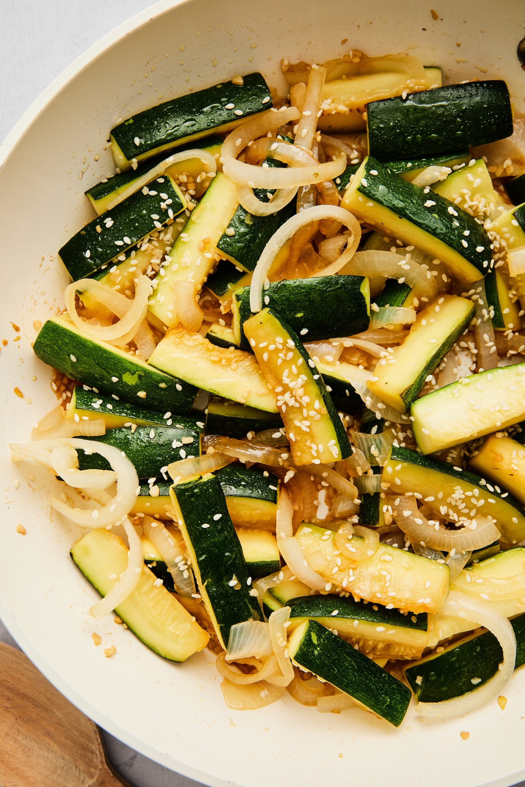 Close-up of sautéed Asian zucchini and onions garnished with sesame seeds in a white skillet.