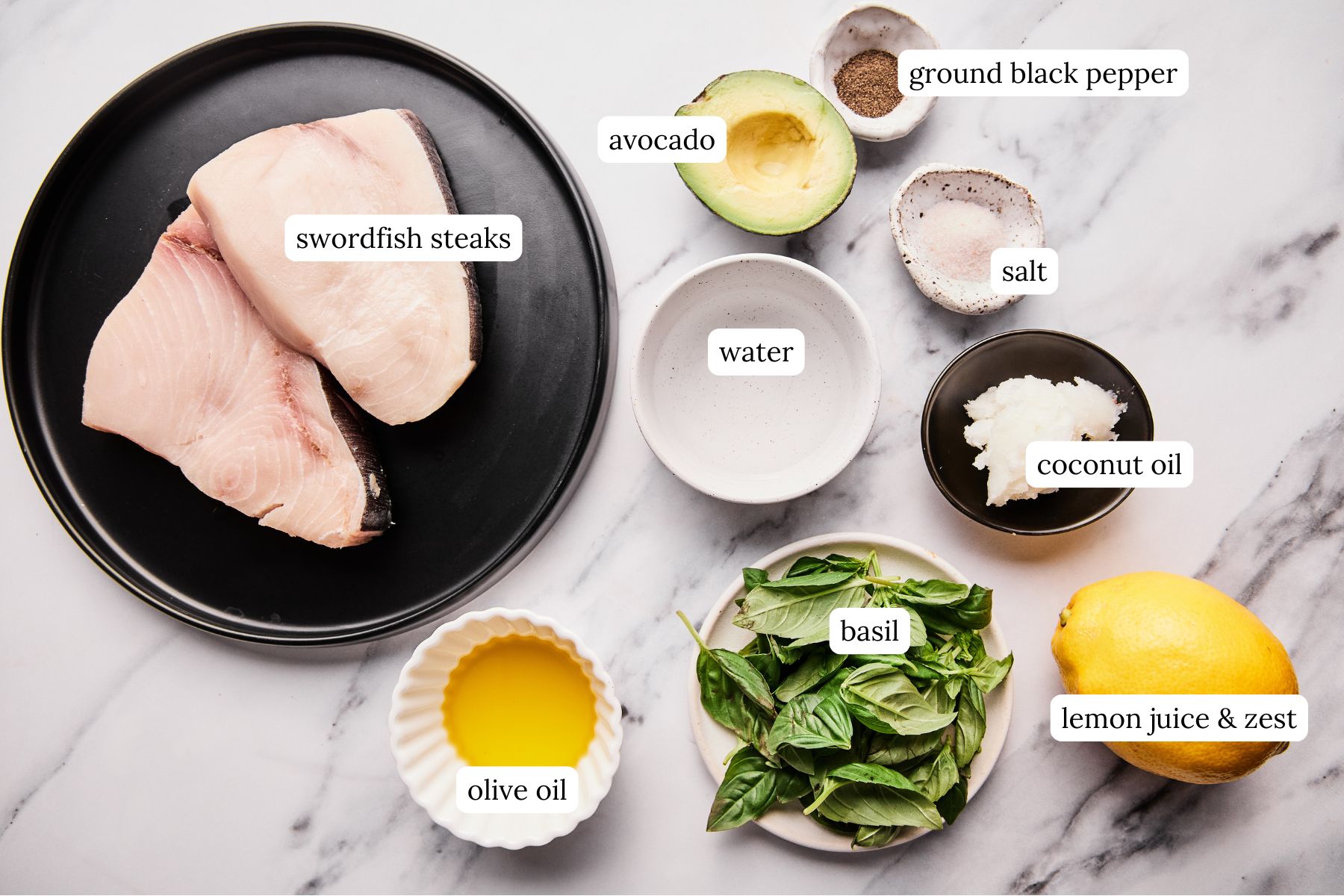Ingredients for swordfish steak recipe with creamy lemon basil sauce labeled and laid out on a white and gray marble looking countertop.
