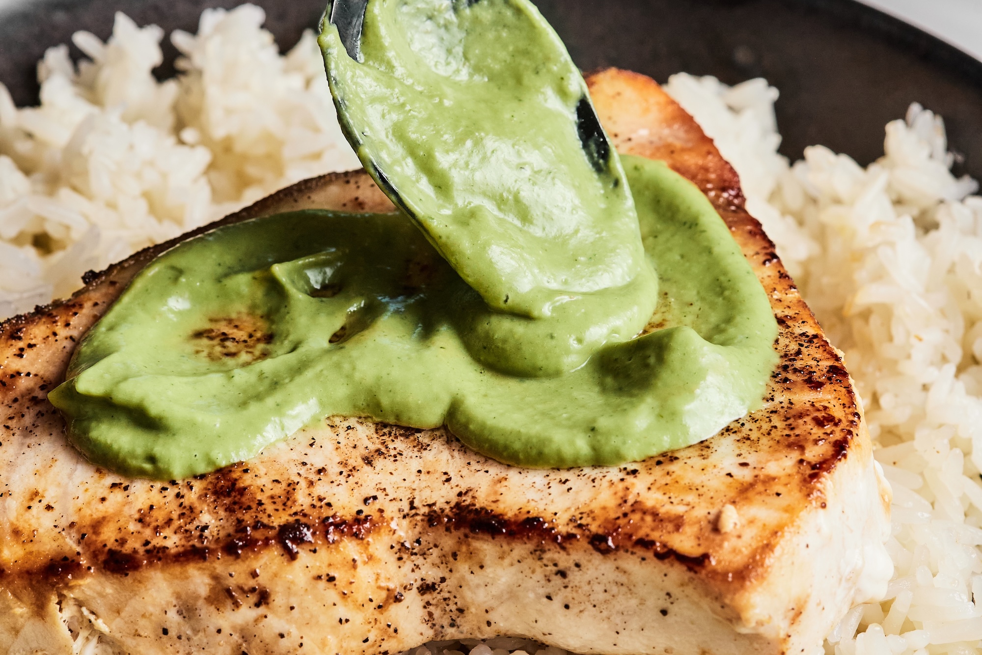 A swordfish steak atop a bed of rice and covered in lemon basil sauce.