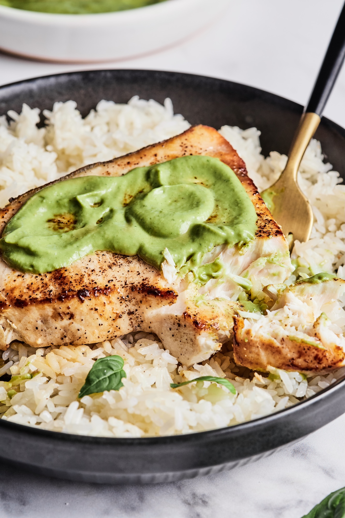 A swordfish steak atop a bed of rice and covered in lemon basil sauce with a piece cut out.