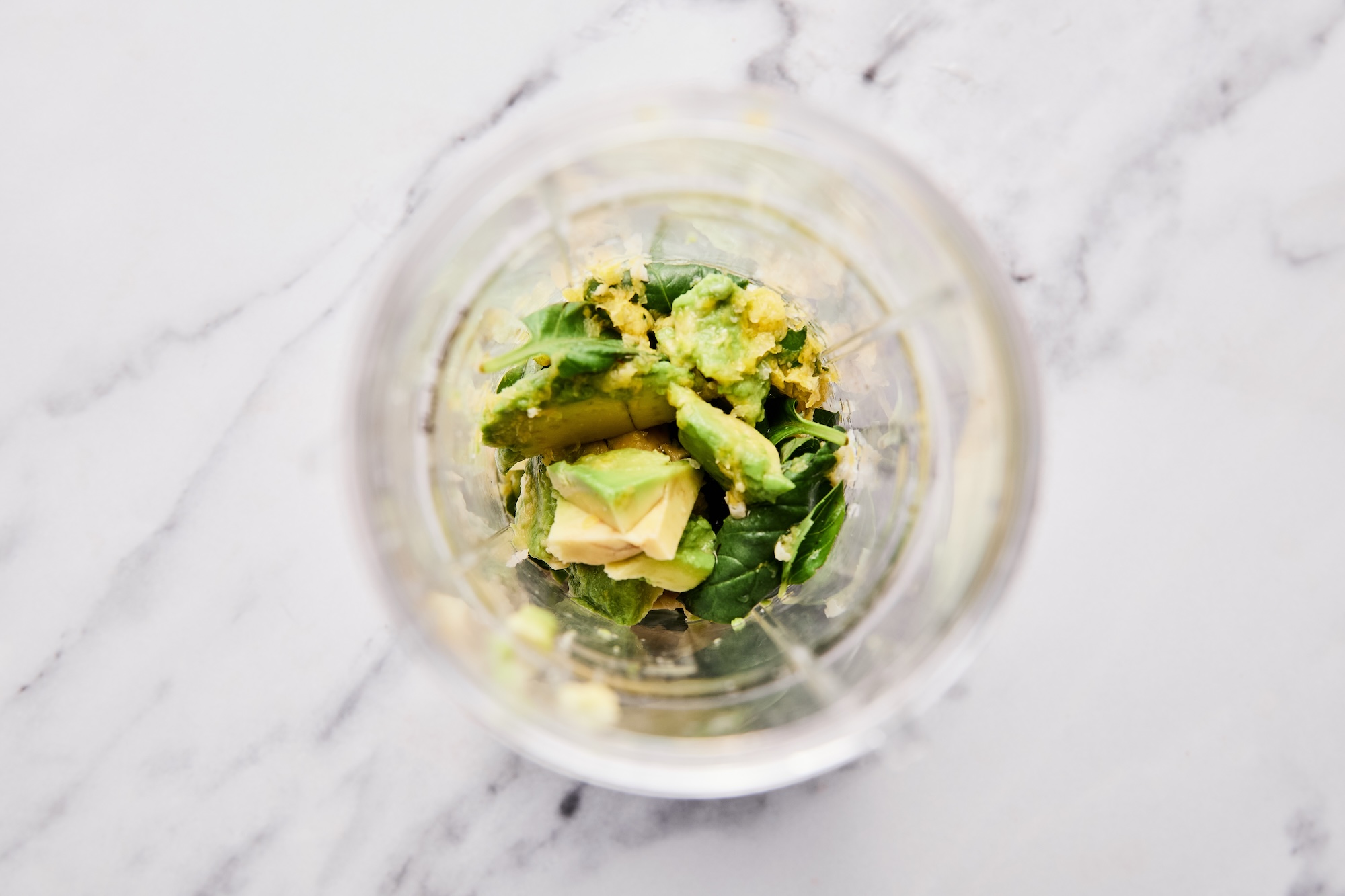 Avocado, basil, lemon zest and juice, olive oil, and water in a glass mixing bowl.