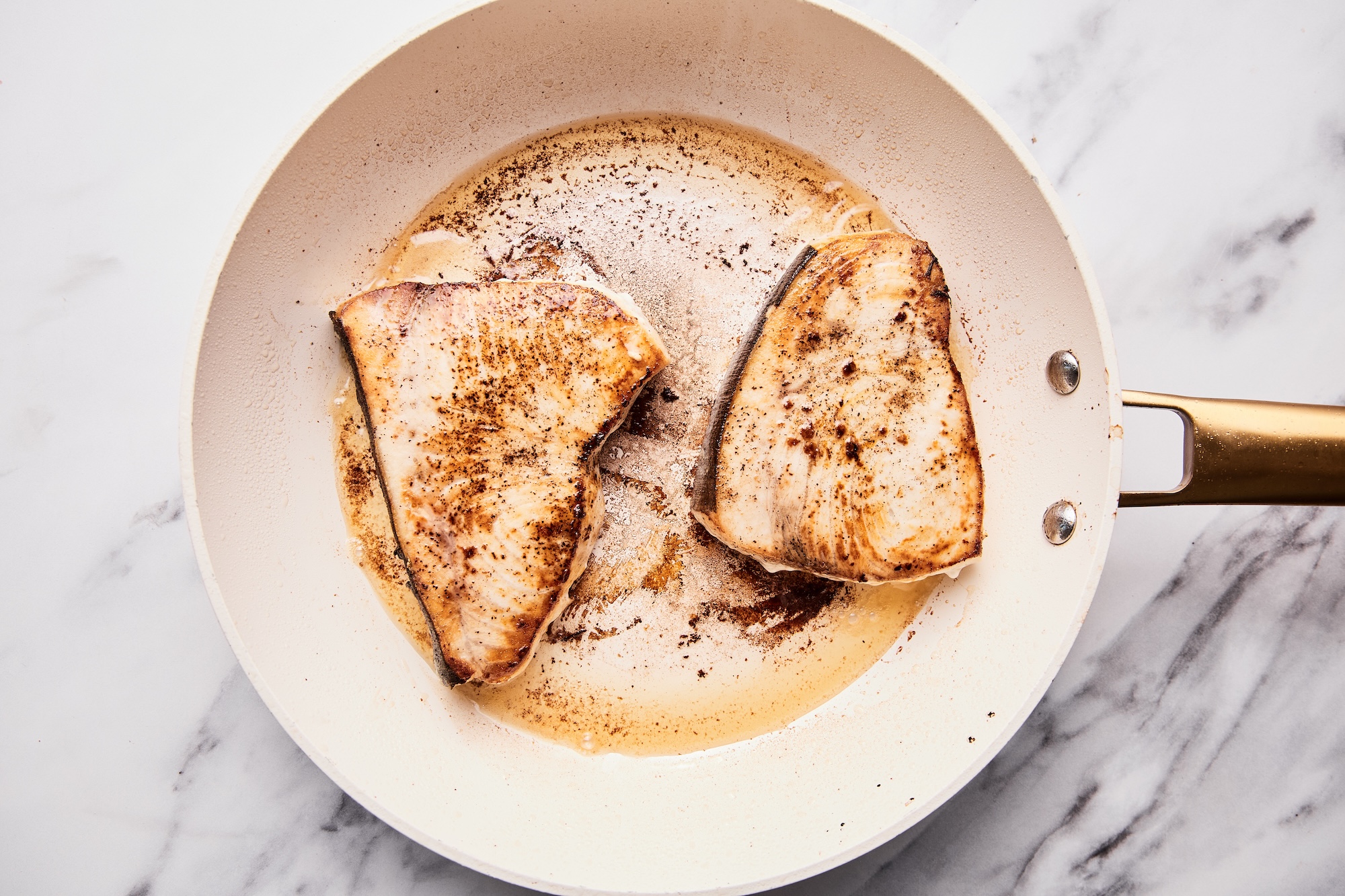 Swordfish steaks in cast iron skillet cooking - the golden crust visible.