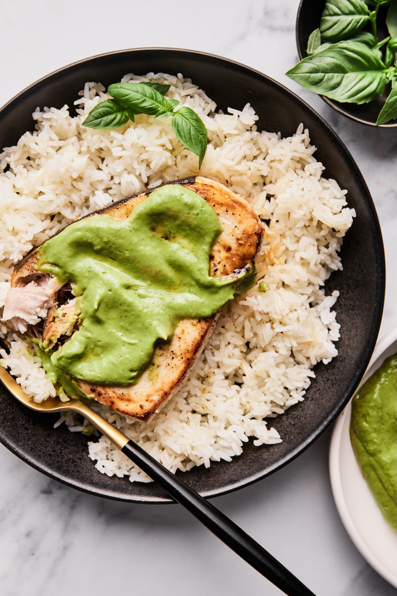 Swordfish steak recipe with creamy lemon basil sauce laid atop a bed of rice on a black plate.
