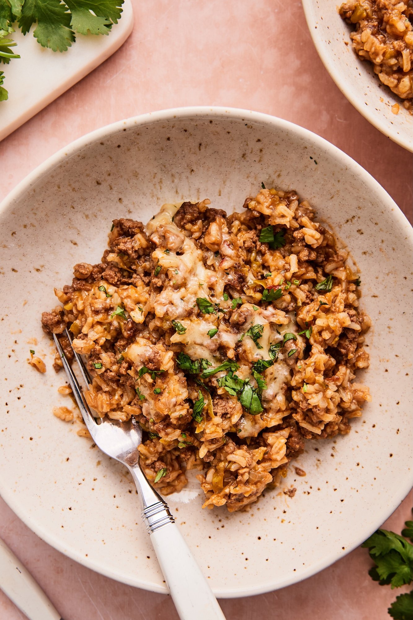 A bowl of ground beef and rice skillet with a fork, ready to eat on a pink background.