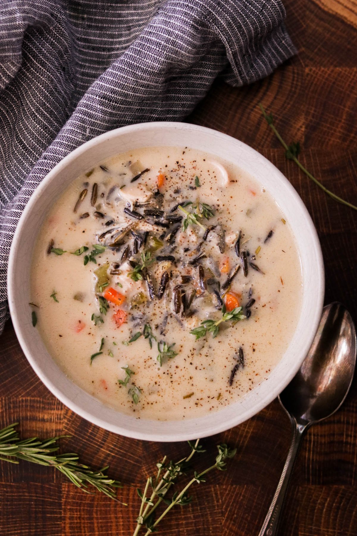 Chicken and wild rice soup in a bowl sitting on a wooden cutting board with a blute and white striped dish towel next to it.